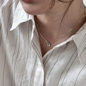 Minimalist silver geometric pendant necklace on model wearing a striped linen shirt