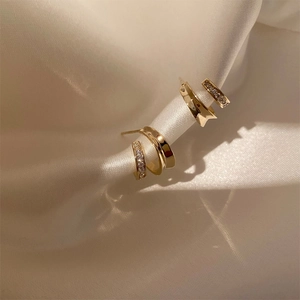 Zweilagige goldene C-förmige Ohrstecker mit Zirkonia-Mikroeinlage auf weißem Seidenhintergrund