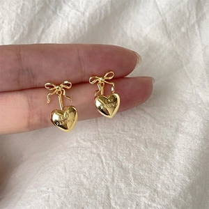 Detail of gold bow earrings with heart pendant featuring EAR PARTNER engraving