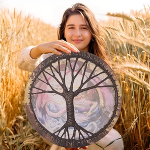 Detail of shamanic drum with tree of life and dragon design in a golden wheat field