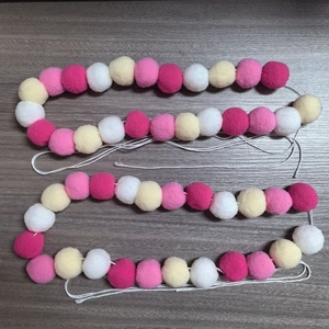 Gros plan d'une guirlande de pompons en peluche rose, jaune et blanc sur bois