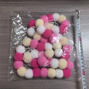 Détail de guirlande de pompons roses et blancs emballée avec ruban à mesurer