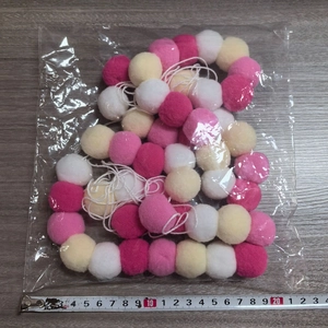 Guirlande de pompons 2m blanc et rose emballée avec un ruban à mesurer à côté