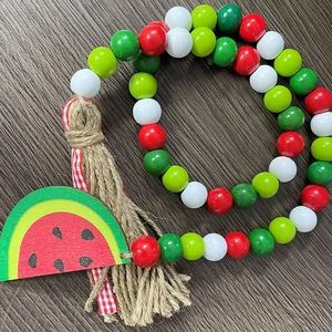 Detailed view of watermelon wood bead garland with rustic jute tassel and plaid ribbon