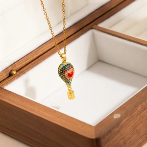 Collier montgolfière doré avec zircons colorés posé sur un écrin à bijoux en bois