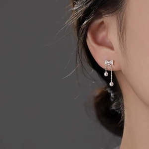 Elegant bow pearl tassel earrings in silver finish on model against dark background