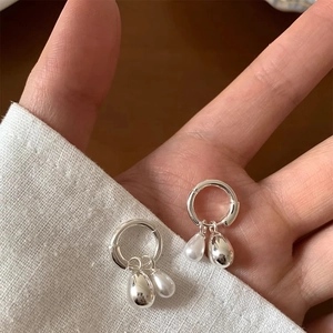 Minimalist silver hoop earrings with water drop pearls and metal charms shown in hand