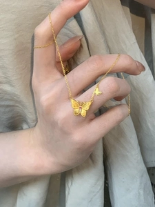 Détails d'un collier papillon doré avec cristal rose tenu à la main sur fond beige