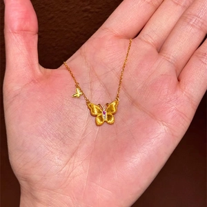 Collier avec pendentif papillon doré, pierre précieuse rouge et finition mate sur main
