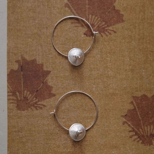 Silver mushroom pendant hoop earrings with radial texture on vintage leaf paper background