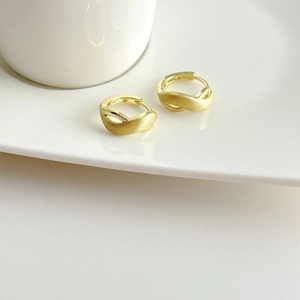 Elegant gold crossover hoop earrings with brushed matte finish on a white ceramic tray