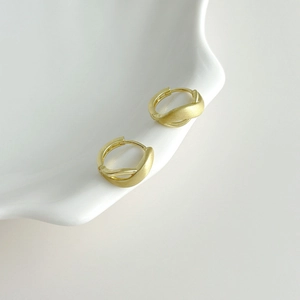 Minimalist matte gold crossover twist hoop earrings on a white ceramic plate