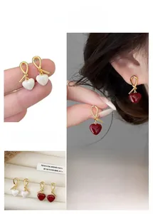 Detail of red heart drop earrings with gold knotted design and pearl white variant