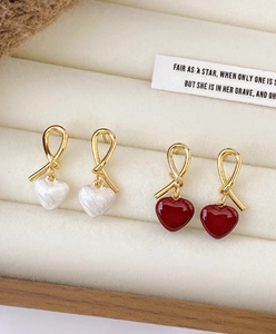 Detailed close-up of knotted gold stud earrings with red and white pearl heart pendants