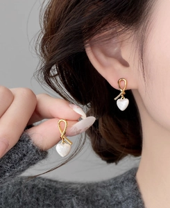 Detailed view of heart-shaped earrings featuring gold knots and mother-of-pearl texture