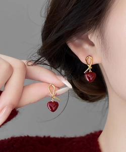 Detail view of heart shaped earrings with gold knot design and red enamel pendants