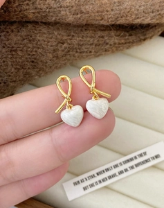 Detail of gold ribbon knot earrings featuring white marble-textured heart pendants