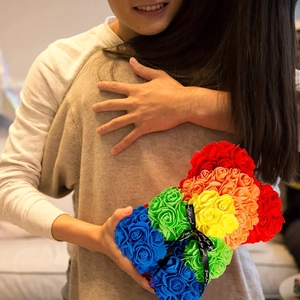 Close-up of rainbow preserved rose bear with black ribbon bow in a romantic hug scene