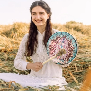 Detail of bohemian shaman drum with colorful goddess pattern being held in a wheat field