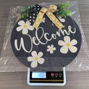 Detail shot of round wooden Welcome sign with floral patterns on electronic scale weighing 196g