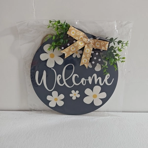 Close-up of farmhouse welcome sign with white script text and artificial daisy greenery