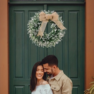 Green artificial wreath with burlap bow and white flowers on a dark green front door