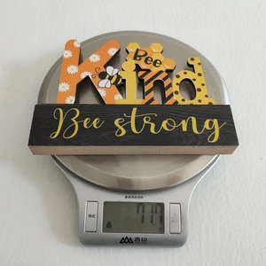 Bee Kind wooden ornament on digital scale showing weight of 71.7 grams for decor