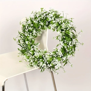 Corona de follaje verde artificial con flores blancas apoyada en una silla blanca