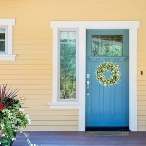 Corona de flores blancas artificiales con hojas verdes en una puerta de entrada azul