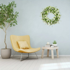Corona de flores blancas artificiales en pared azul sobre un sofá amarillo