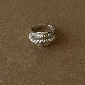 Silver lip-shaped open ring with twisted rope detail on a textured brown background