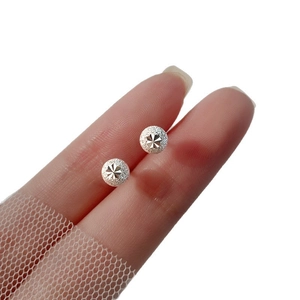 Frosted silver spherical stud earrings with engraved star pattern held by fingers