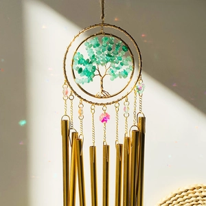 Detail of life tree wind chime with green crystals, golden metal tubes and light bokeh