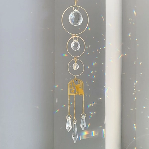 Hanging crystal suncatcher with golden cat frame casting rainbow light on a grey wall