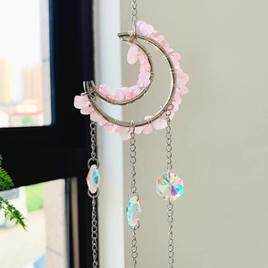 Detail of moon-shaped pink crystal dreamcatcher with hanging iridescent heart pendants