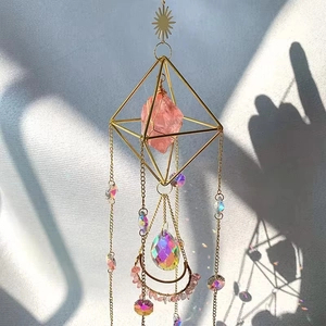 Close-up of pink crystal stone in a geometric gold frame with moon and sun charms