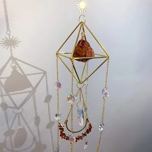 Close-up of golden octahedral wind chime with red gemstone and moon charm detail