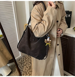 Close-up of a large brown suede tote bag with a cute teddy bear charm on the strap