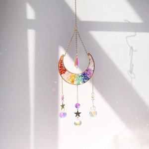 Macro shot of moon shaped crystal suncatcher with chakra stones casting rainbow shadows