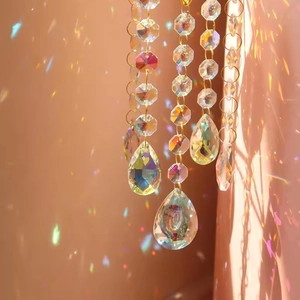 Crystal suncatcher with faceted teardrop prisms creating rainbow light on a soft warm backdrop