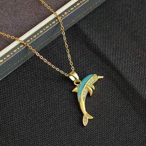 Collier dauphin doré avec émail vert et zircons sur un présentoir texturé gris