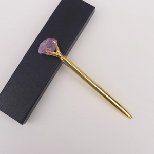 Gros plan du stylo à bille doré avec cristal brut violet et son coffret cadeau noir
