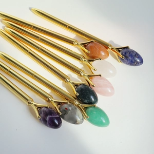 Golden metal ballpoint pens set with various oval semi-precious gemstones on a white background