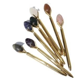 Seven gold metal ballpoint pens with unique natural crystal stone tops on white background