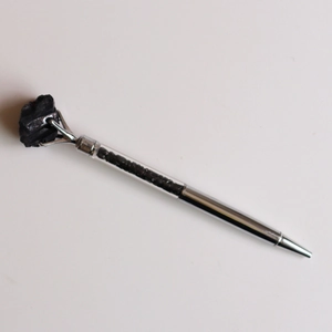 Détail macro d'un stylo à bille en argent avec pierre brute noire et cristaux concassés