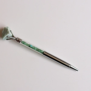 Détail d'un stylo bille argenté avec cristal brut vert et remplissage de pierres assorties