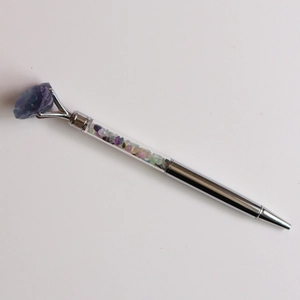 Détail d'un stylo à bille argenté avec des pierres concassées et une pointe en cristal violet