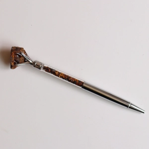 Détail d'un stylo à bille argenté avec tube transparent rempli de pierres brunes