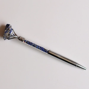 Détail d'un stylo à bille argenté avec cristaux bleus et pointe en pierre naturelle brute