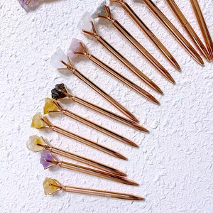 Rose gold metal ballpoint pens topped with natural crystal raw stones on white background